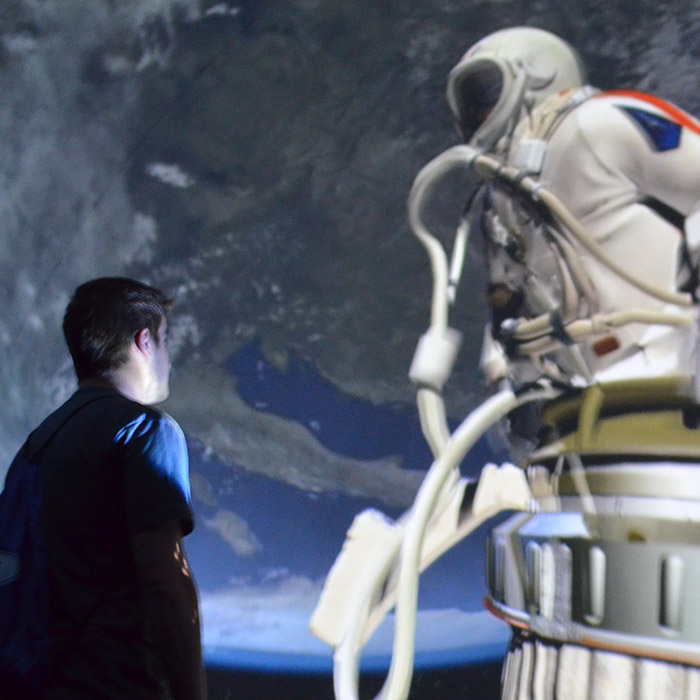 A young man stands inside of the portable planetarium and gazes at a projection of a simulated space mission.