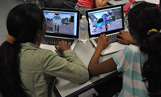 Two girls in the GROOVE program sit at laptops and work to create their virtual simulations.