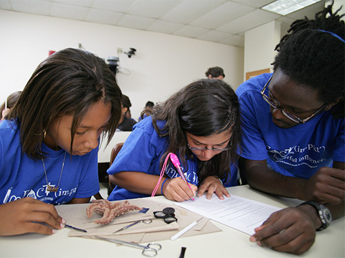 Two girls assess and take notes on the structure of a starfish as a mentor looks on.