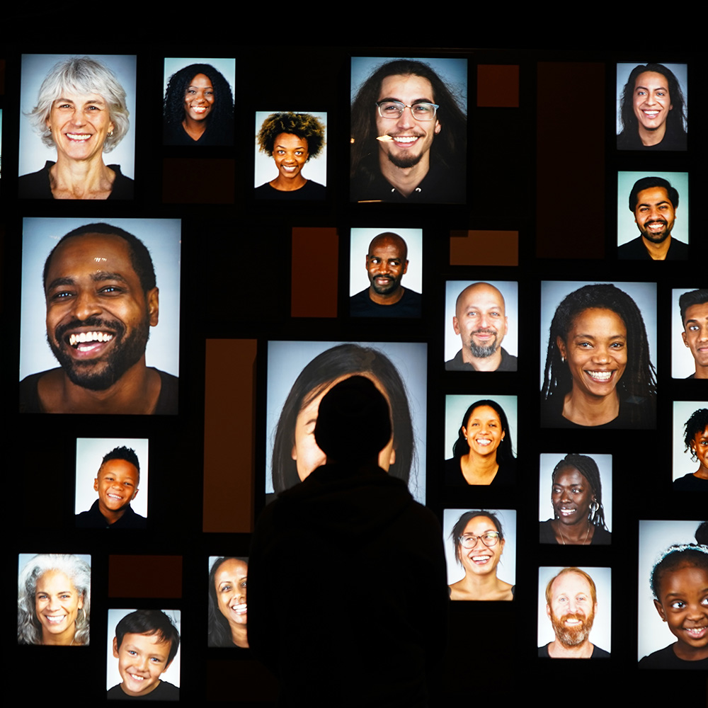 Wall of photos of faces in Photo of Skin: Living Armor, Evolving Identity exhibition.