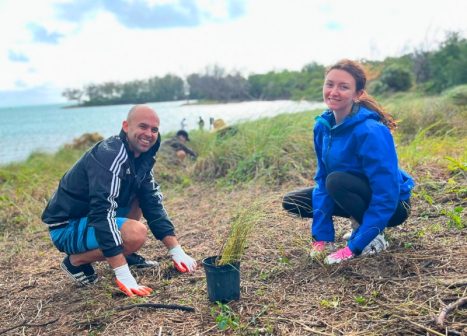 Woman and man crouching on the ground in a coastal habitat using tools to plant a native species.
