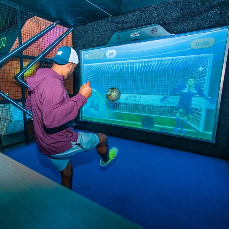 man kicking a ball towards a screen with a virtual soccer goalie