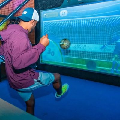 man kicking a soccer ball at a screen projection of a goal