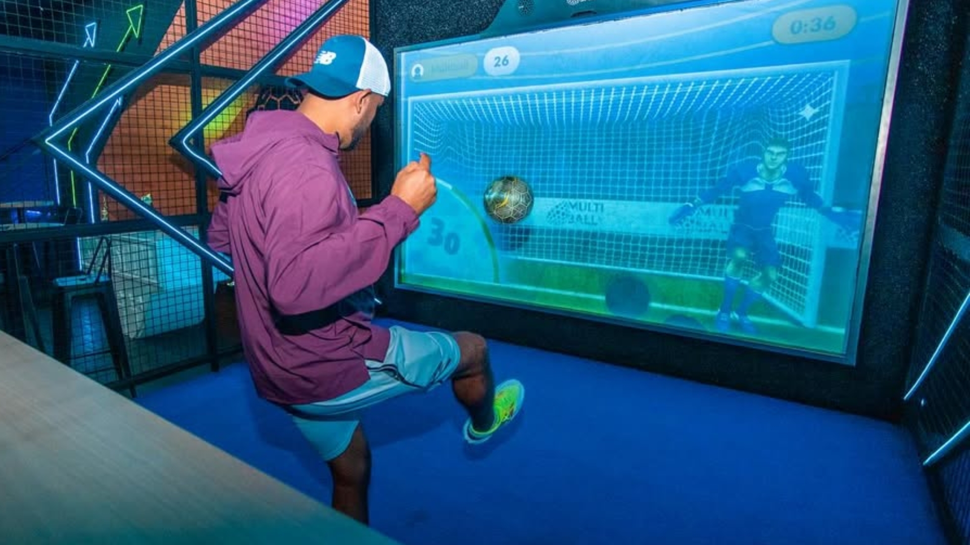 man kicking a soccer ball at a screen projection of a goal